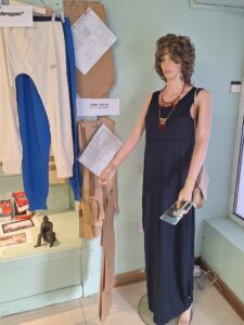 **Alt text:** Display featuring a black John Rocha dress made in Balbriggan, shown on a mannequin alongside textile patterns, archival materials and traditional Balbriggan stockings as part of the “A Stitch in Time” exhibition. 