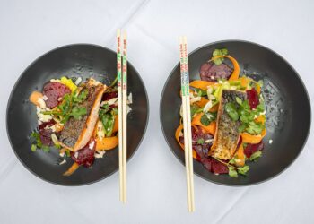 Two black bowls containing pan-seared salmon fillets served with vibrant vegtables and chopsticks.