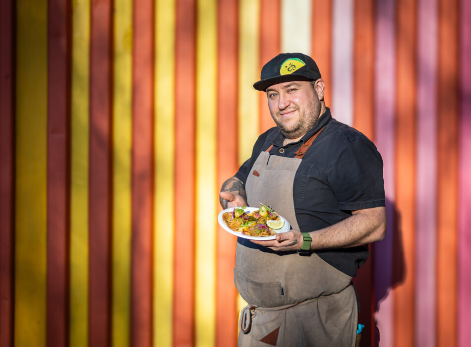 Jeremy Cuevas of La Cocina Cuevas posing with cusine infront of a colourful background.