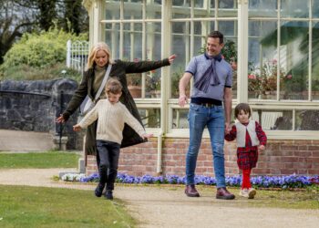 A family of four walking happily along a stone path outside Ardgillan greenhouse conservatory.