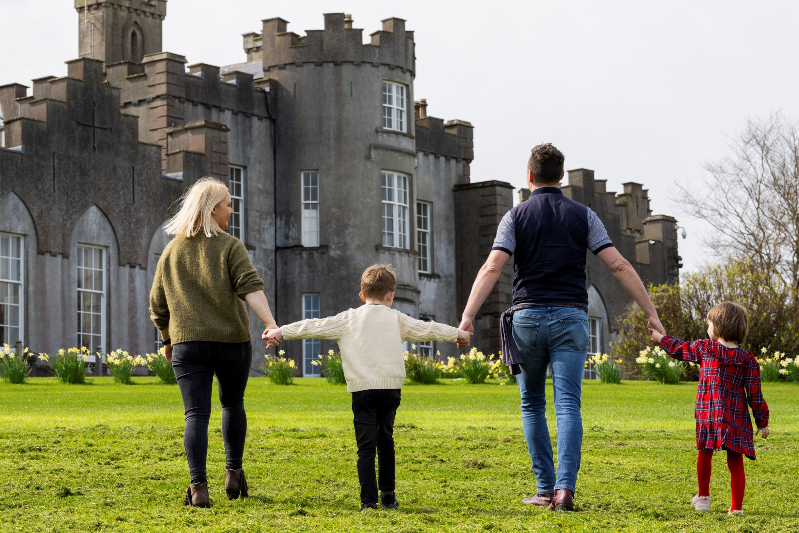 A family of four holding hands while walking on the lawn towards Ardgillan Castle.
