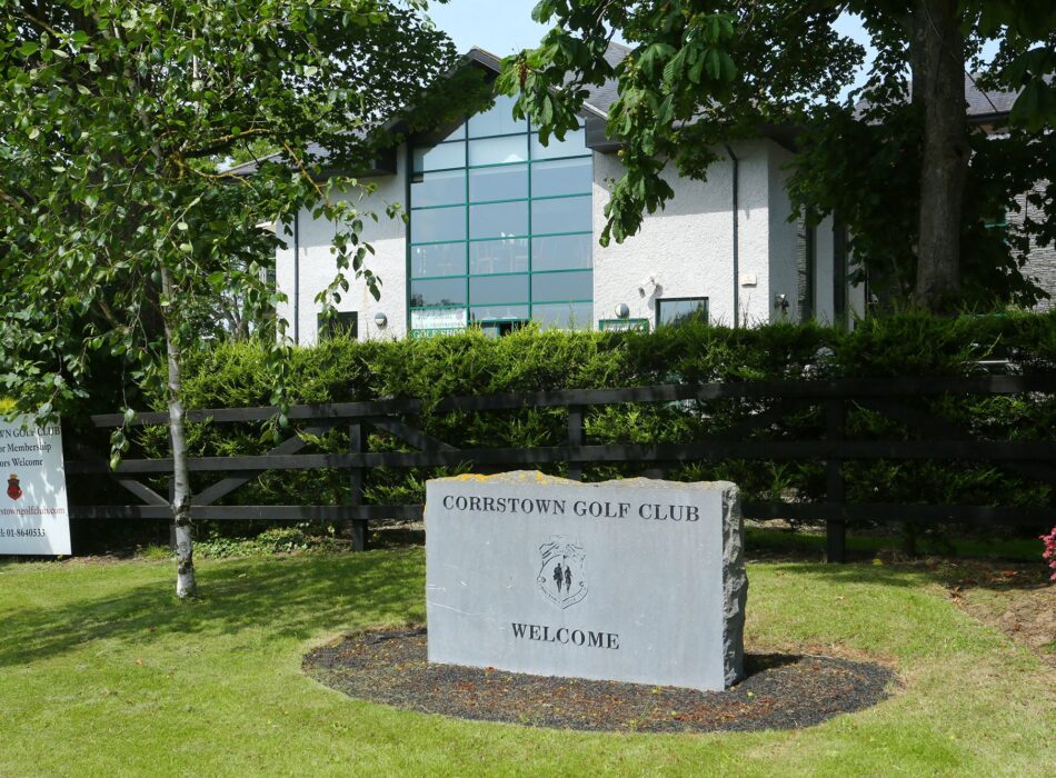 The entrance to Corrstown Golf Club, featuring a stone welcome sign set among landscaped gardens with the modern clubhouse visible behind mature trees. The peaceful setting offers a warm welcome to members and visitors enjoying one of Fingal's scenic parkland golf courses.