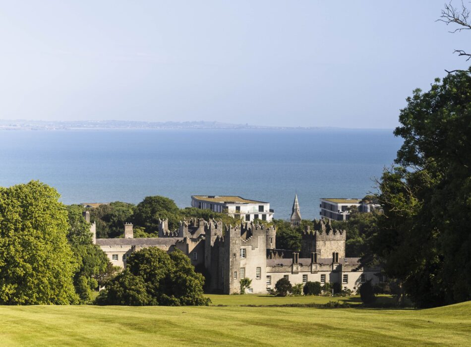 Historic greystone castle nestled among lush green fairways set against a vast, calm blue sea.