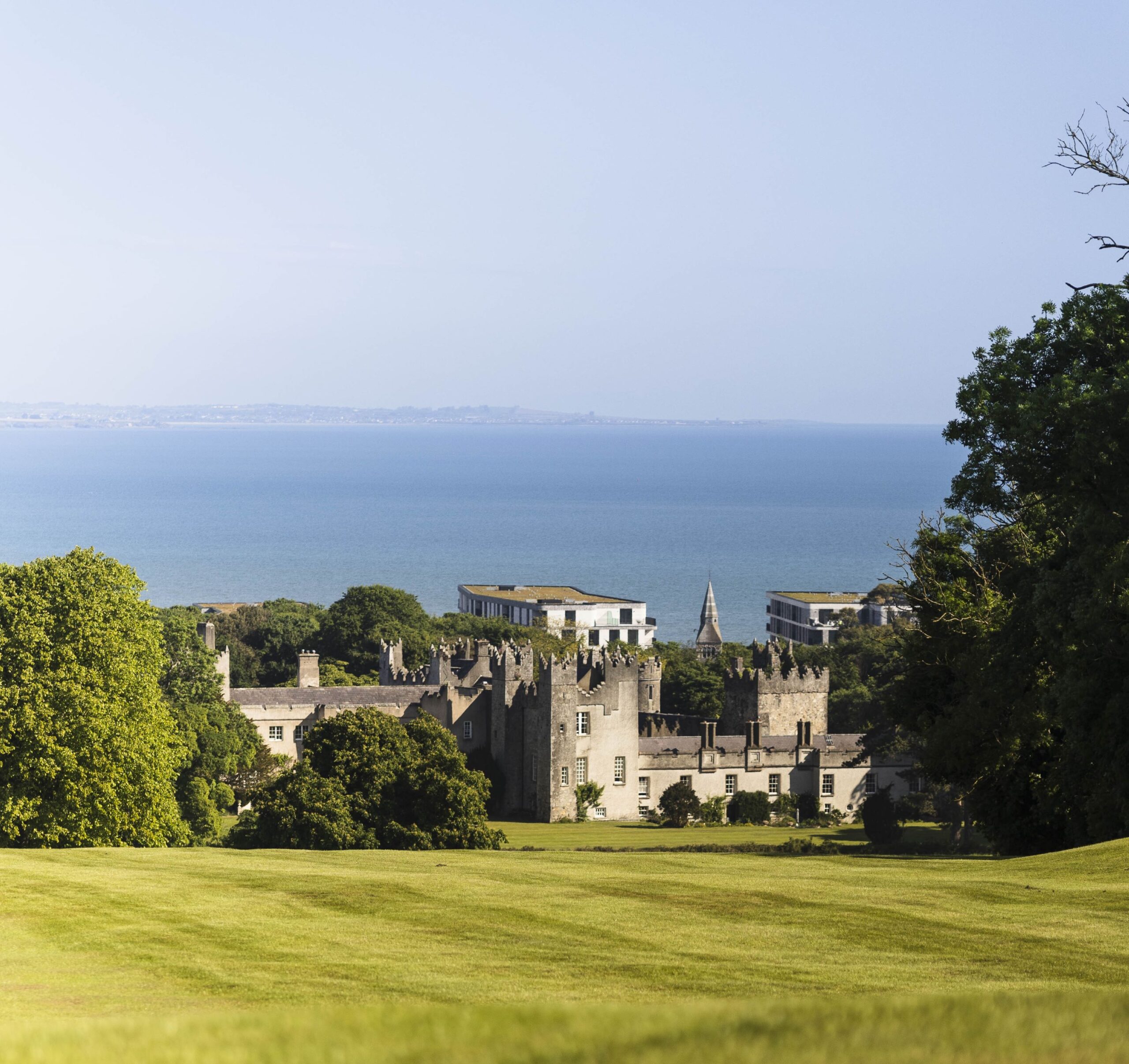 Historic greystone castle nestled among lush green fairways set against a vast, calm blue sea.