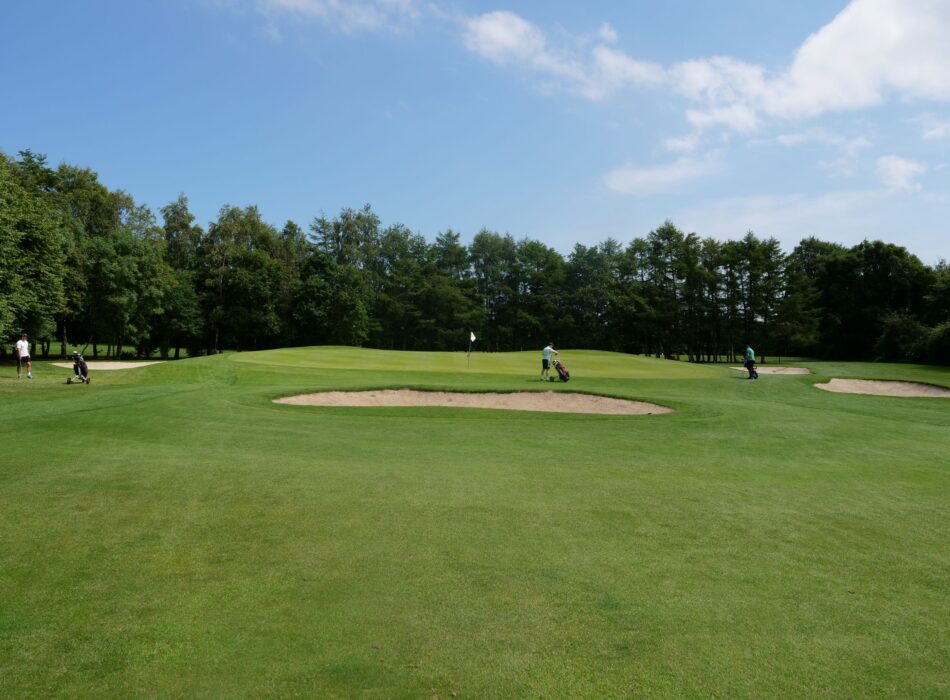 lmgreen golf club fairway under a cloudy sky, while a group of golfers stands near a tea area.