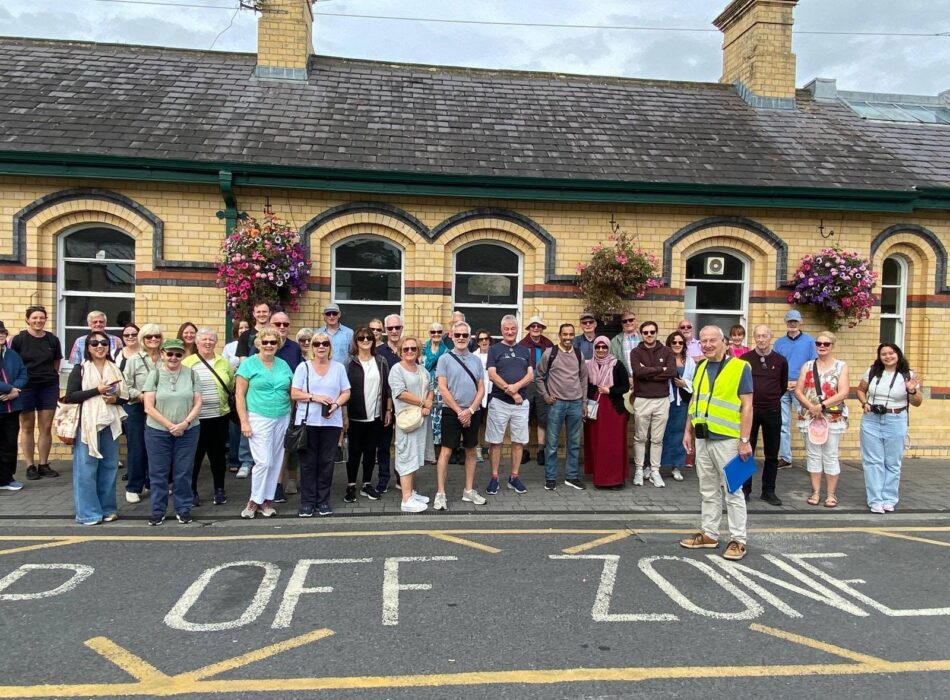 A large group of people posing for a group photo in a designated drop-off zone outside a historic brick building.