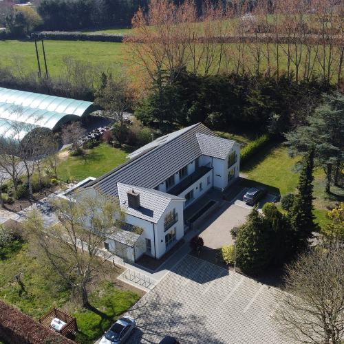 Aerial view of Hidden Acres, featuring a modern white two-storey house surrounded by gardens, mature trees and green countryside.